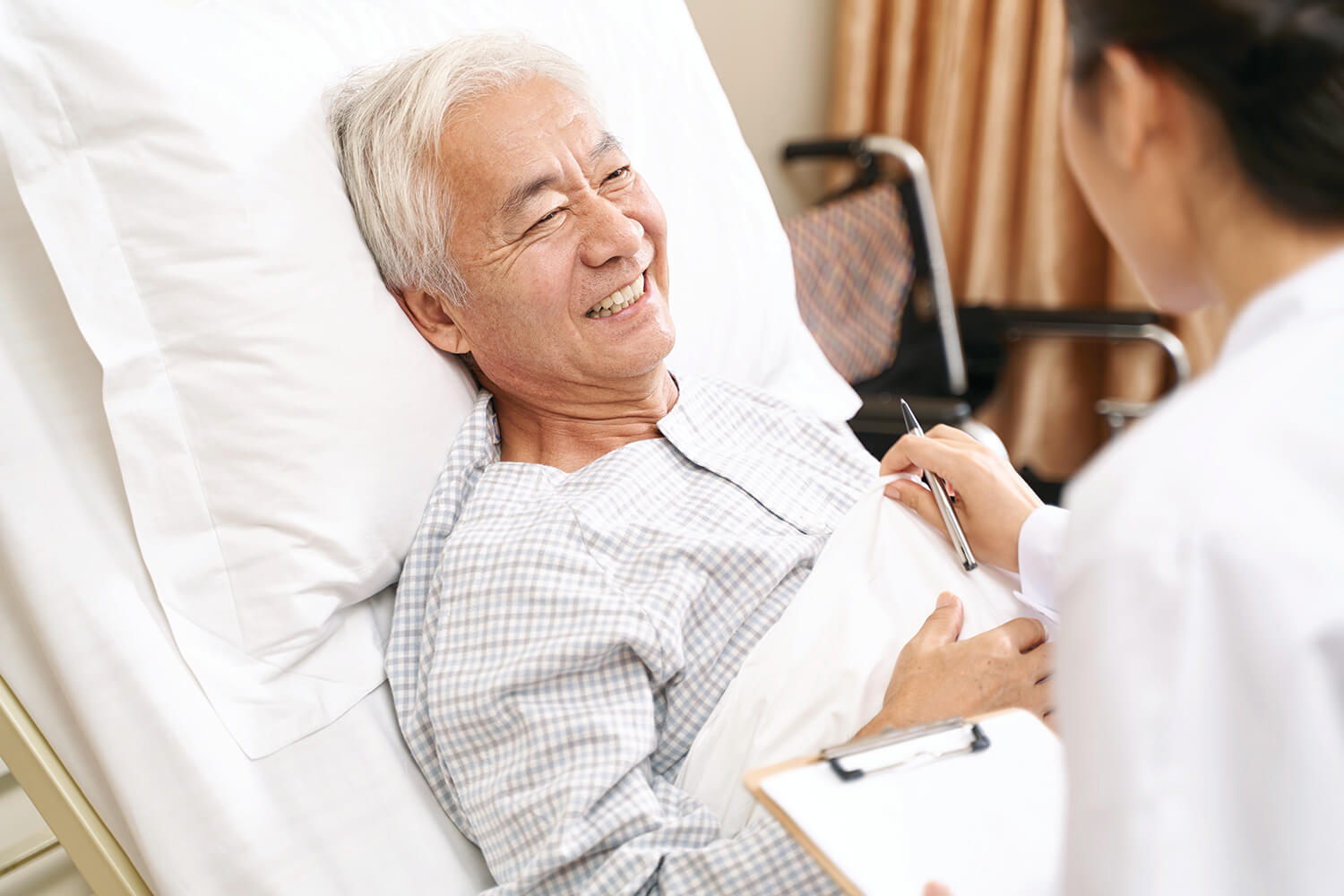 senior asian patient talking to caretaker in hospital ward